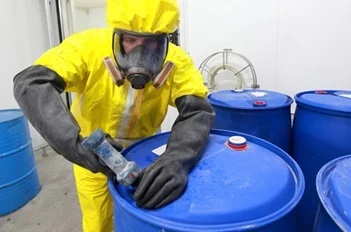 Worker in yellow hazmat suit sealing a barrel of chemicals.